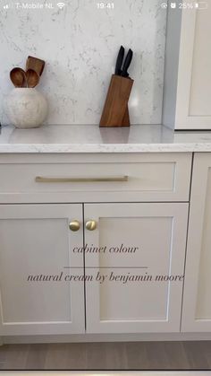 a kitchen with white cabinets and wooden utensils on the counter top in front of a marble tile backsplash