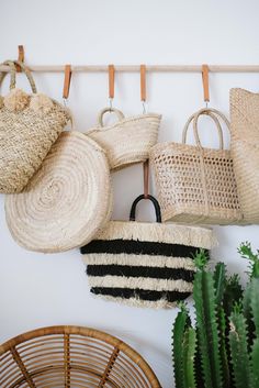 several straw bags hanging on a wall next to a cactus