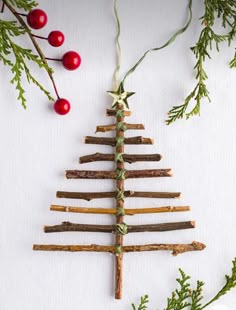 a christmas tree made out of sticks and branches with berries on the table next to it