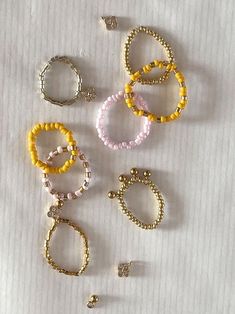 several different colored bracelets and rings on a white tablecloth with gold beading