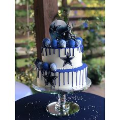 a three tiered cake decorated with blue and white icing, topped with a football helmet