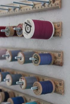 several spools of thread are hanging on a wall with measuring tape attached to them