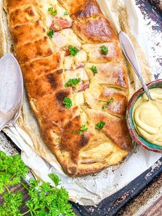 a large piece of bread with meat and vegetables on it next to a bowl of dip