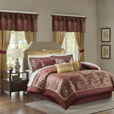 a bed with red and gold comforters in a bedroom next to windows, rugs and lamps