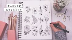 a person holding a pen next to a notebook with flower doodles on the cover