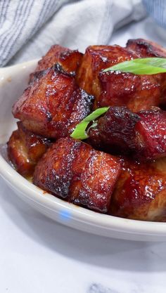 a white bowl filled with cooked meat and garnished with green onions on top