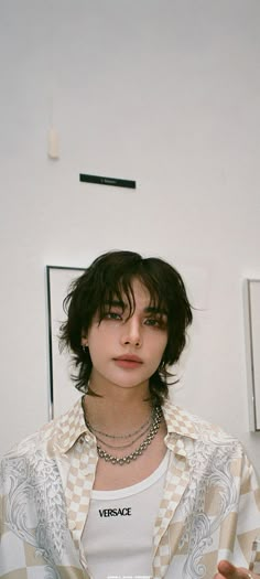 a woman with short hair wearing a checkered shirt and silver necklace standing in front of a white wall