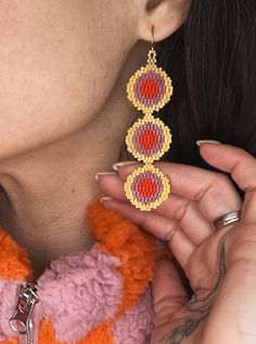 a close up of a person holding a pair of earrings in front of her face