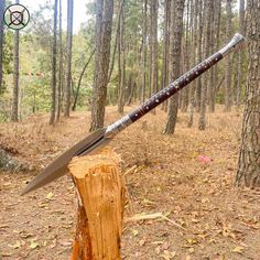 a large knife sitting on top of a piece of wood in the middle of a forest