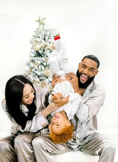 a man and woman holding a baby in front of a christmas tree with a bottle