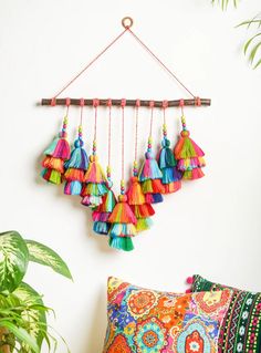 colorful tassels hanging on a wall next to a pillow and potted plant