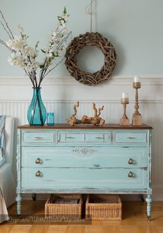 a blue dresser with flowers on top and a wreath hanging above it in a room