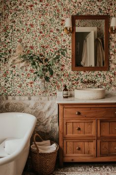 a bathroom with floral wallpaper and an old fashioned bathtub in the foreground