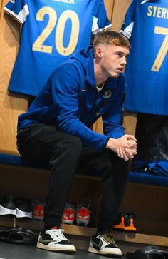 a man squatting down in front of a locker room with shoes on the floor