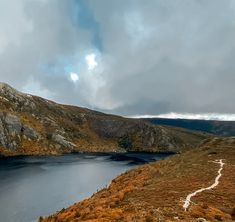 a large body of water surrounded by grass and mountains with clouds in the sky above