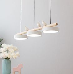 three birds on a branch hanging from the ceiling above a table with flowers and vases