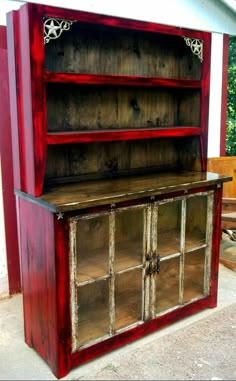 an old red bookcase with glass doors on the front and back sides is sitting outside