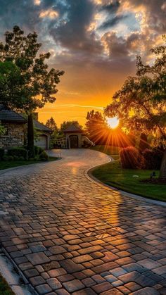 the sun is setting over a cobblestone road in front of some trees and bushes