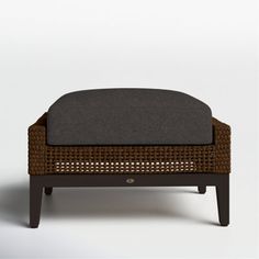 the foot stool is made out of wicker and has a black cushion on it