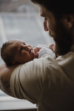 a man holding a baby up to his chest and looking out the window at something outside