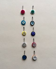 several different colored buttons hanging from hooks on a wall with one button facing the other