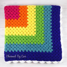 a multicolored crocheted blanket on top of a white wooden surface with the word love written across it