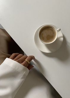 a cup of coffee sitting on top of a white table next to a person's hand