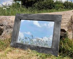 a mirror sitting in the grass next to a fallen tree trunk with clouds reflected in it