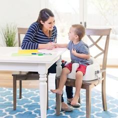 a woman sitting at a table with a little boy in front of her and writing on a piece of paper