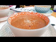 there is a bowl of soup on the table next to two plates with spoons