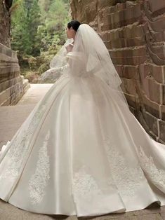 a woman in a wedding dress is standing near a stone wall and wearing a veil