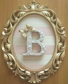 the letter b is made out of pearls and beads in a gold frame on a wall