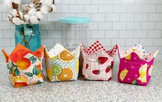 four small fabric houses sitting on top of a counter next to cotton balls and a glass vase