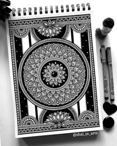 a spiral notebook with black and white art on it next to markers, pens and scissors