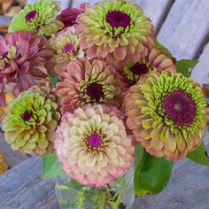 a vase filled with lots of flowers sitting on top of a wooden table next to leaves