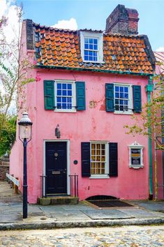 an old pink house with black shutters and red tile on the roof is next to a lamp post