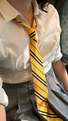 a woman wearing a white shirt and yellow striped tie sitting on a chair with her hands in her pockets