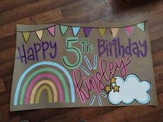 a birthday sign with the number five and rainbows on it, sitting on a wooden floor