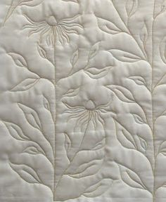 a close up view of a white quilted material with flowers and leaves on it