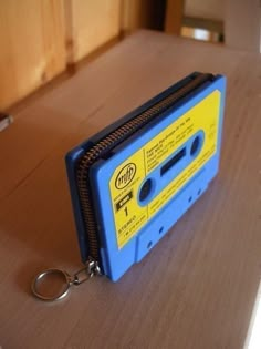 a blue and yellow tape recorder sitting on top of a wooden table next to a metal keychain