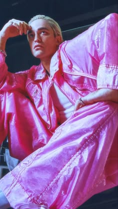 a man sitting on top of a chair wearing a pink raincoat and holding his hand to his head