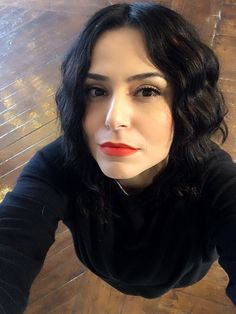 a woman with black hair and red lipstick posing for the camera on a wooden floor