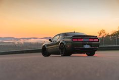 the rear end of a gray sports car driving on a road at sunset with fog in the background