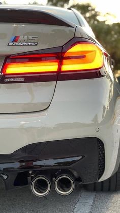 the rear end of a white bmw car with exhaust pipes on it's side