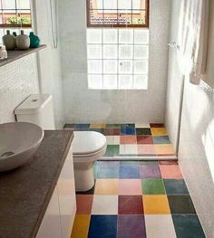 a bathroom with a toilet, sink and colorful tile on the floor in front of a window