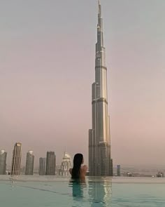 a woman is sitting in the pool looking at the burj