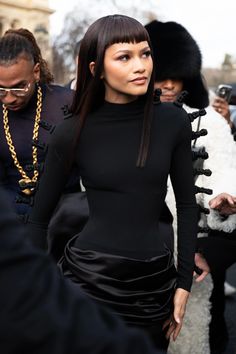 a woman in a black dress is walking through the street with other people behind her