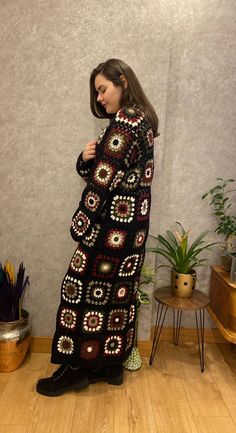 a woman standing in front of a wall wearing a black crocheted sweater and boots