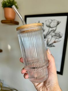 a hand holding a clear glass with a straw in it and a plant behind it