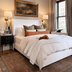 a large white bed sitting in a bedroom next to two lamps and a painting on the wall